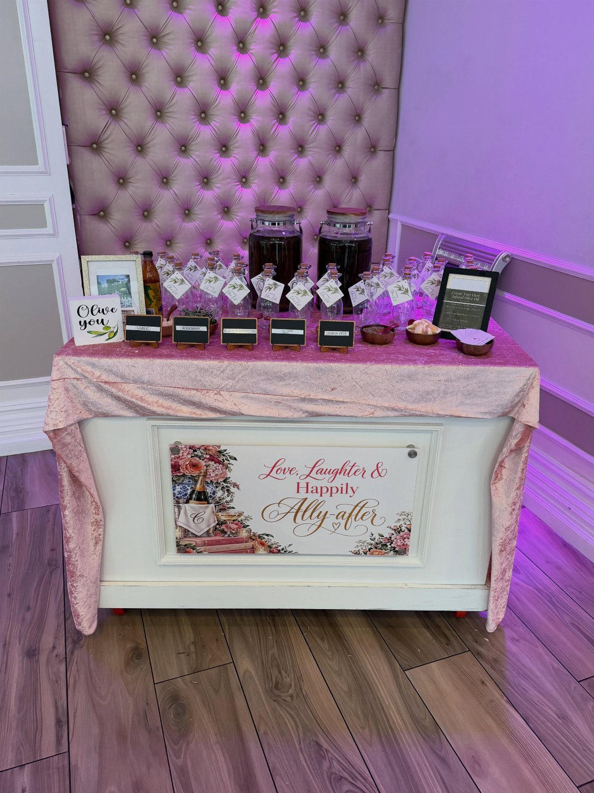 Small glass bottles of infused olive oil on a pink wedding favor table.