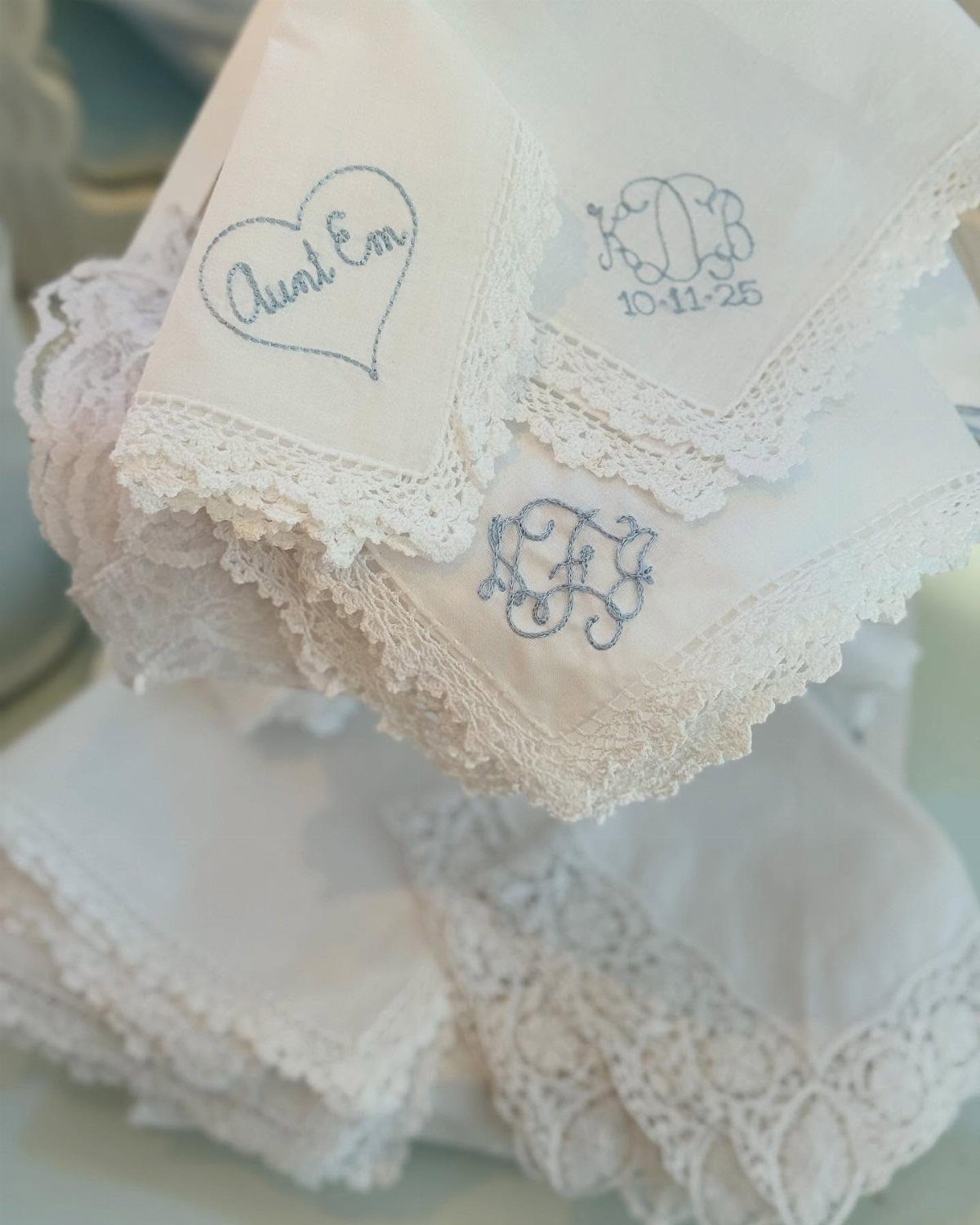 White linen napkins with lace edges and blue embroidered monograms and names.