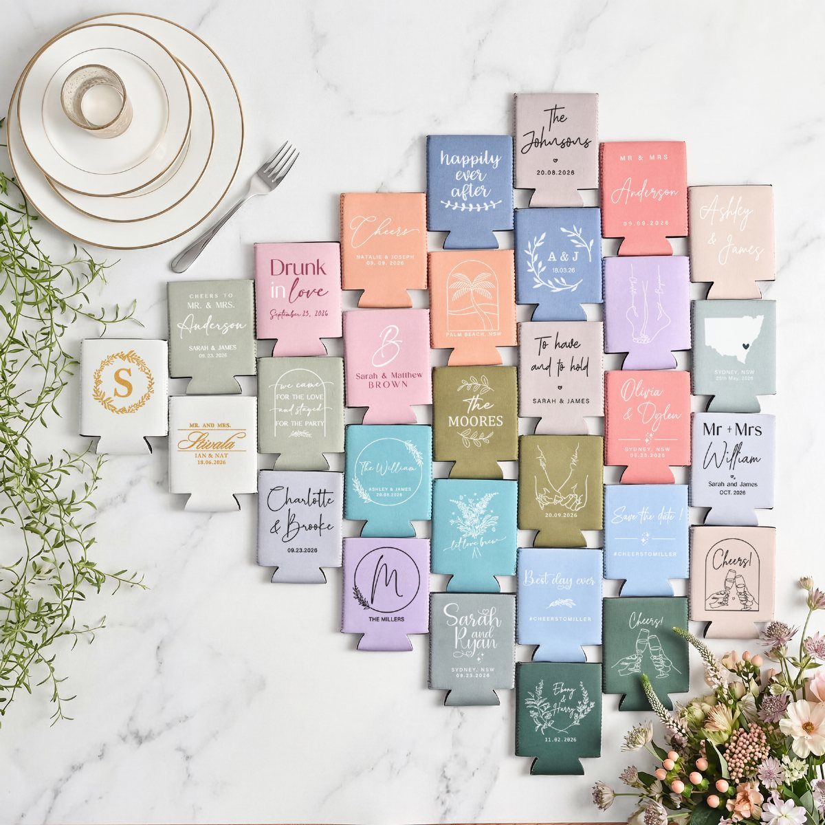 Colorful personalized foam can koozies arranged on a white marble table with dinnerware.