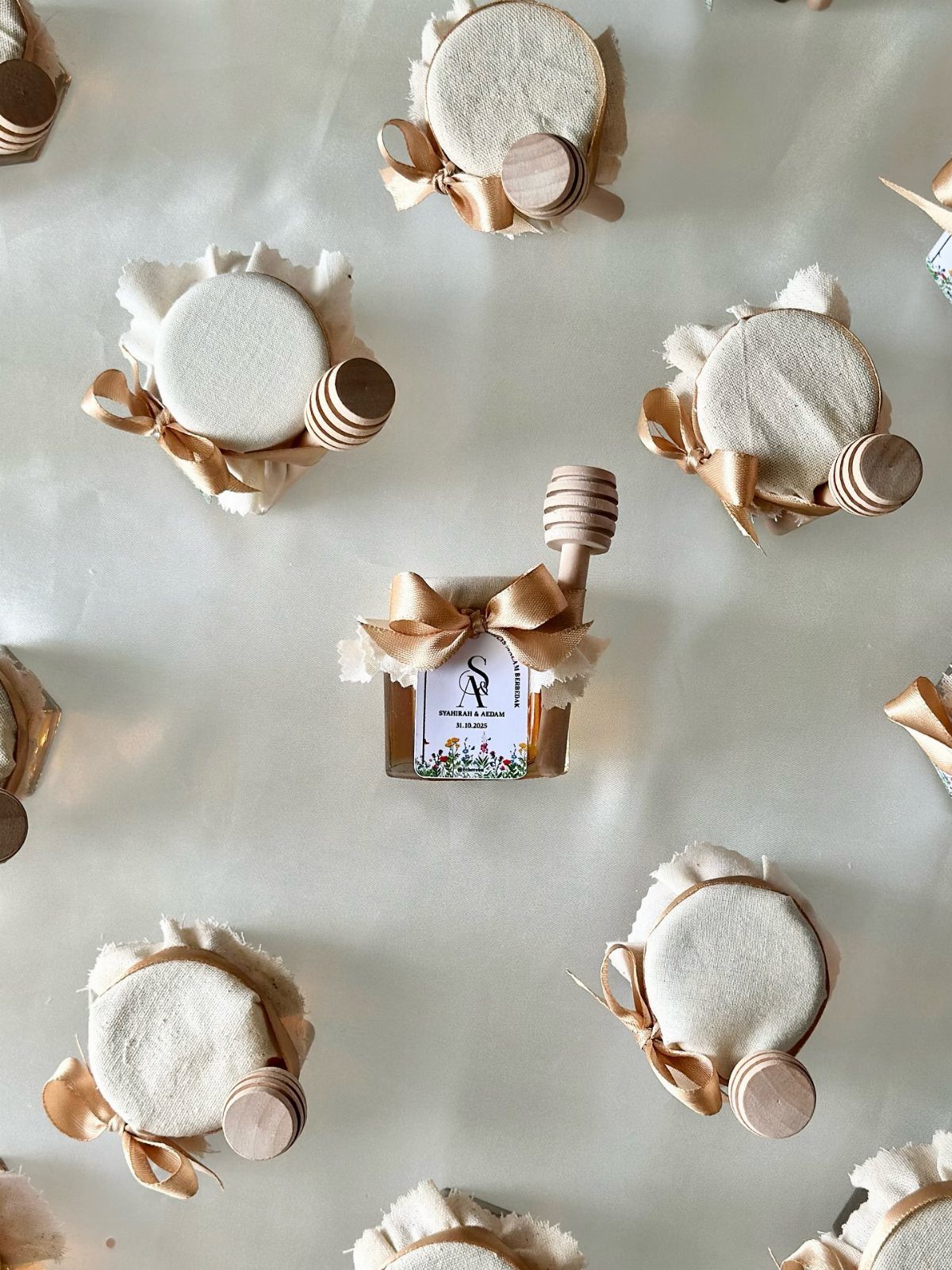 Mini honey jars with white fabric lids, gold ribbons, and wooden honey dippers.