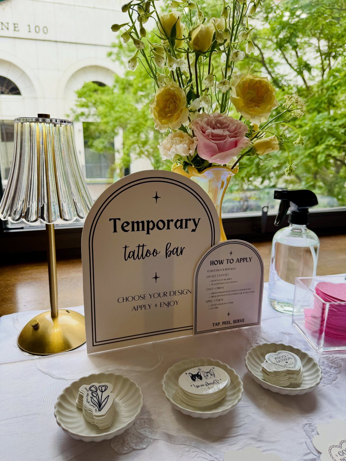 Temporary tattoo bar setup with design plates, instructions, and fresh floral arrangements.