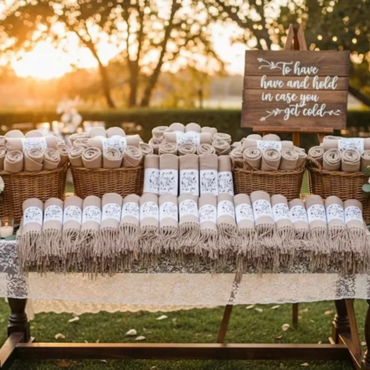 Rolled beige throw blankets with labels on a lace table at an outdoor wedding