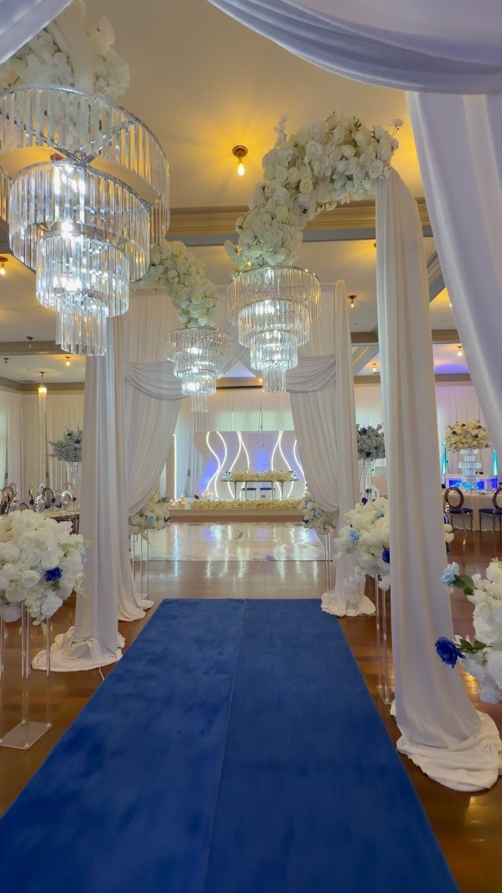 Royal blue aisle runner leading through a white draped wedding venue with chandeliers.