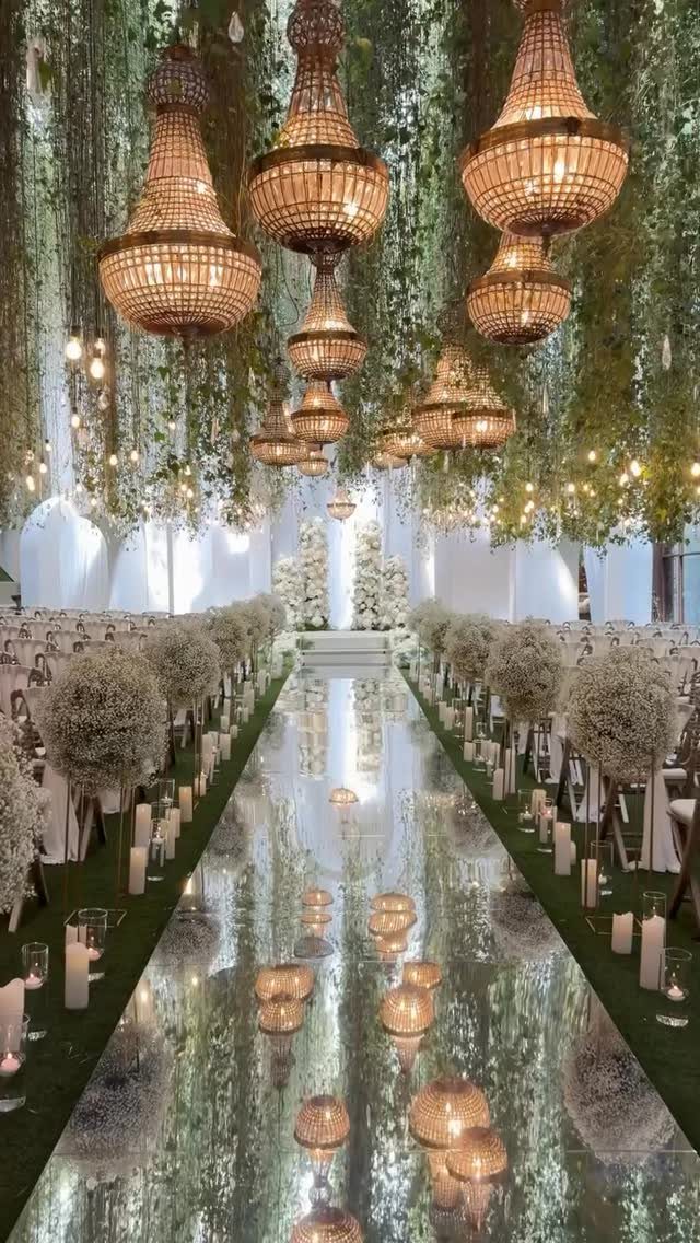 Mirrored wedding aisle lined with white pillar candles, floral spheres, and crystal chandeliers.