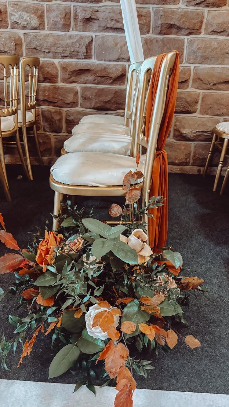 Orange and white floral arrangement on the floor beside gold wedding chairs.