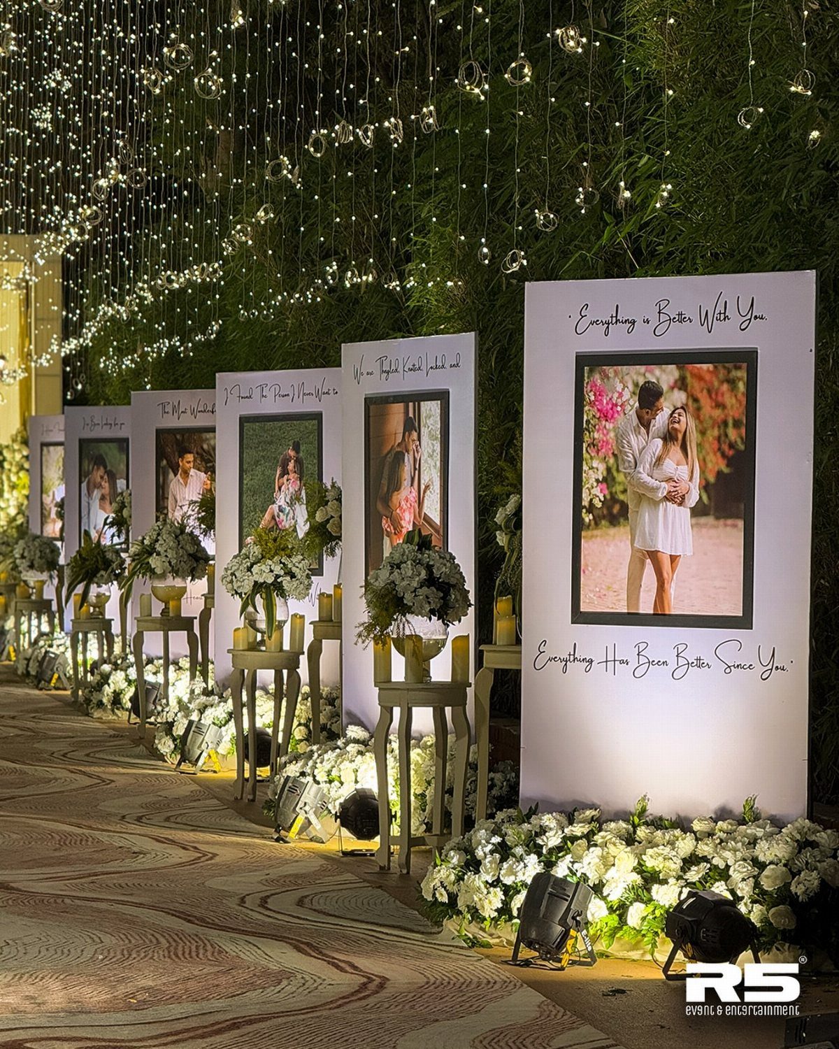 Wedding aisle with framed couple photos on white panels and white floral arrangements.