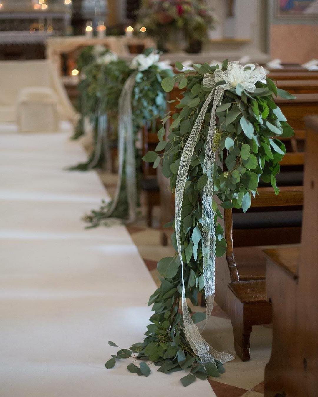 Green eucalyptus garlands with white flowers and silver ribbons on wooden church pews.