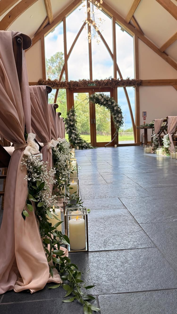 Glass lanterns with white pillar candles and greenery lining a stone wedding aisle.