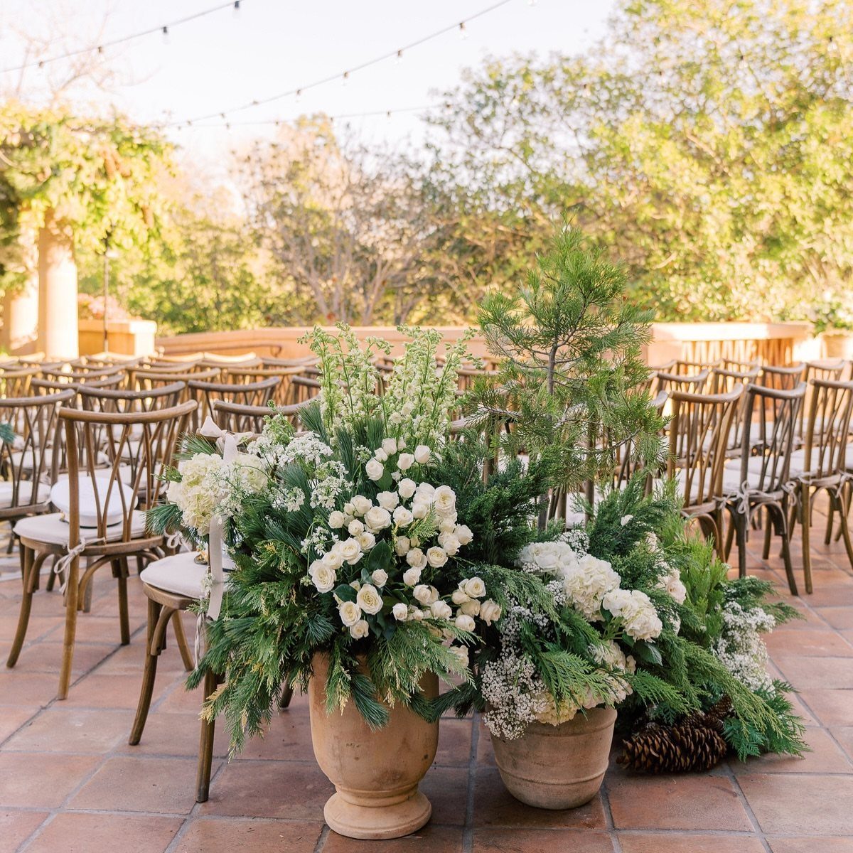 Large terracotta pots with white flowers and greenery lining a wedding aisle.