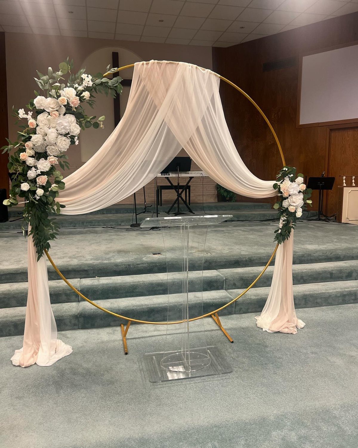 Gold circular wedding arch with white fabric draping and white floral arrangements