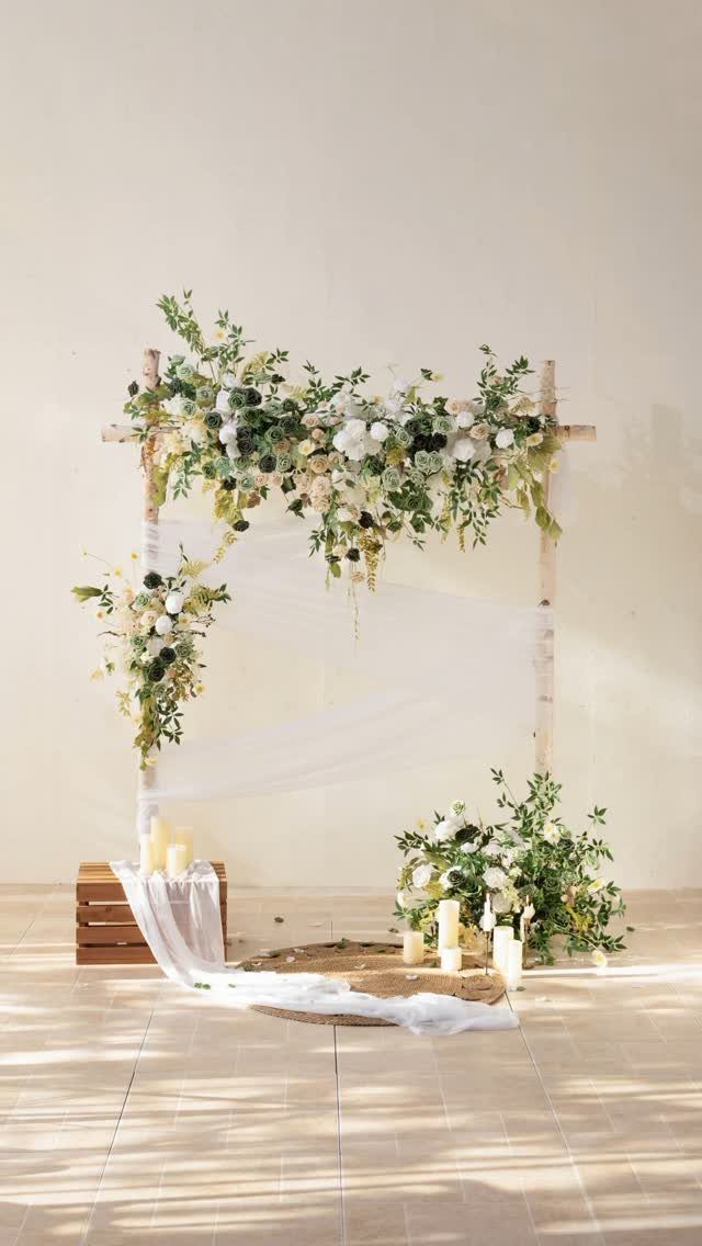 Wooden altar frame decorated with white flowers, greenery, and draped white sheer fabric.