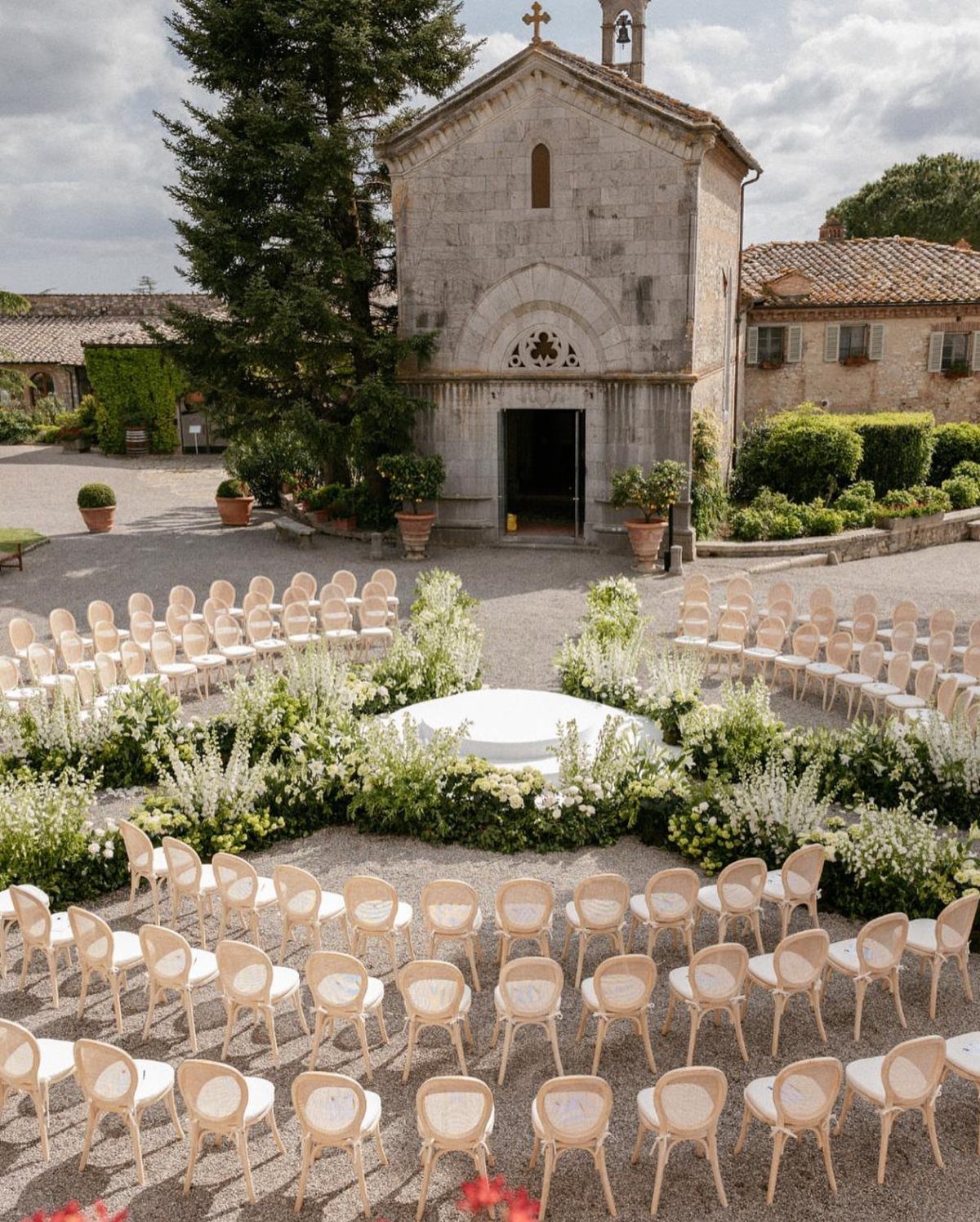 Crescent-shaped white floral ground installation surrounding a circular platform in a stone courtyard.