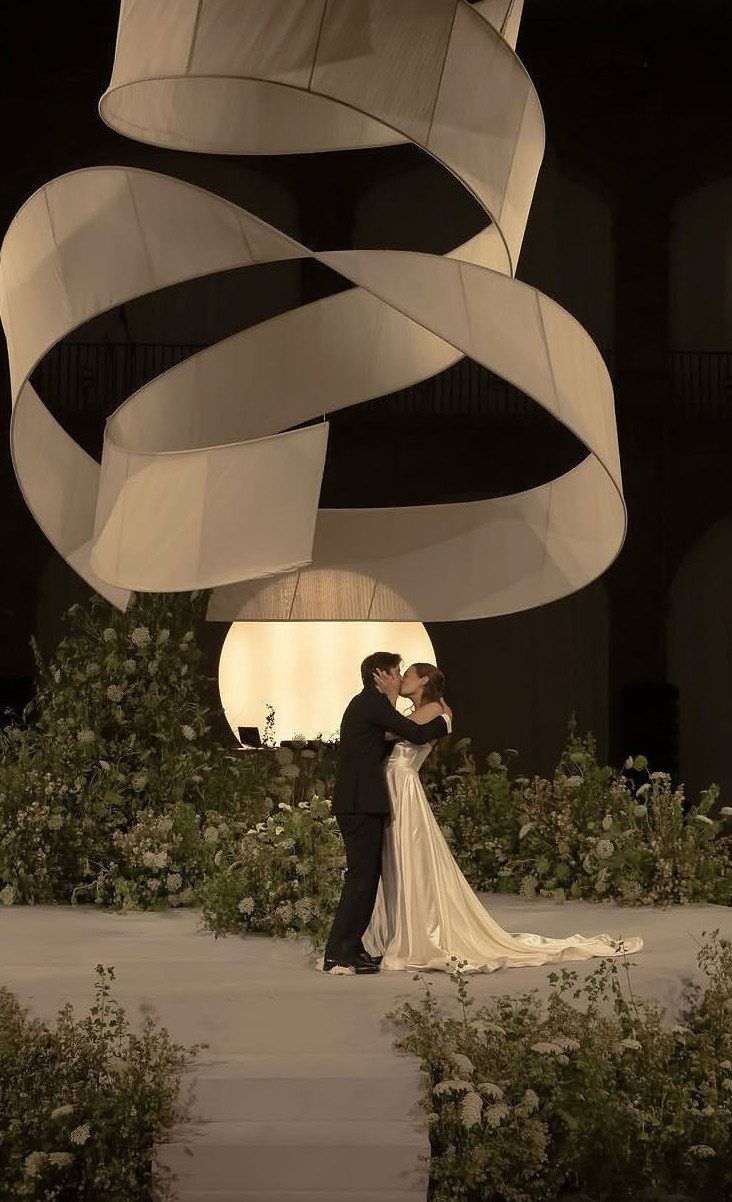 Bride and groom kissing under a large white sculptural geometric altar with flowers.