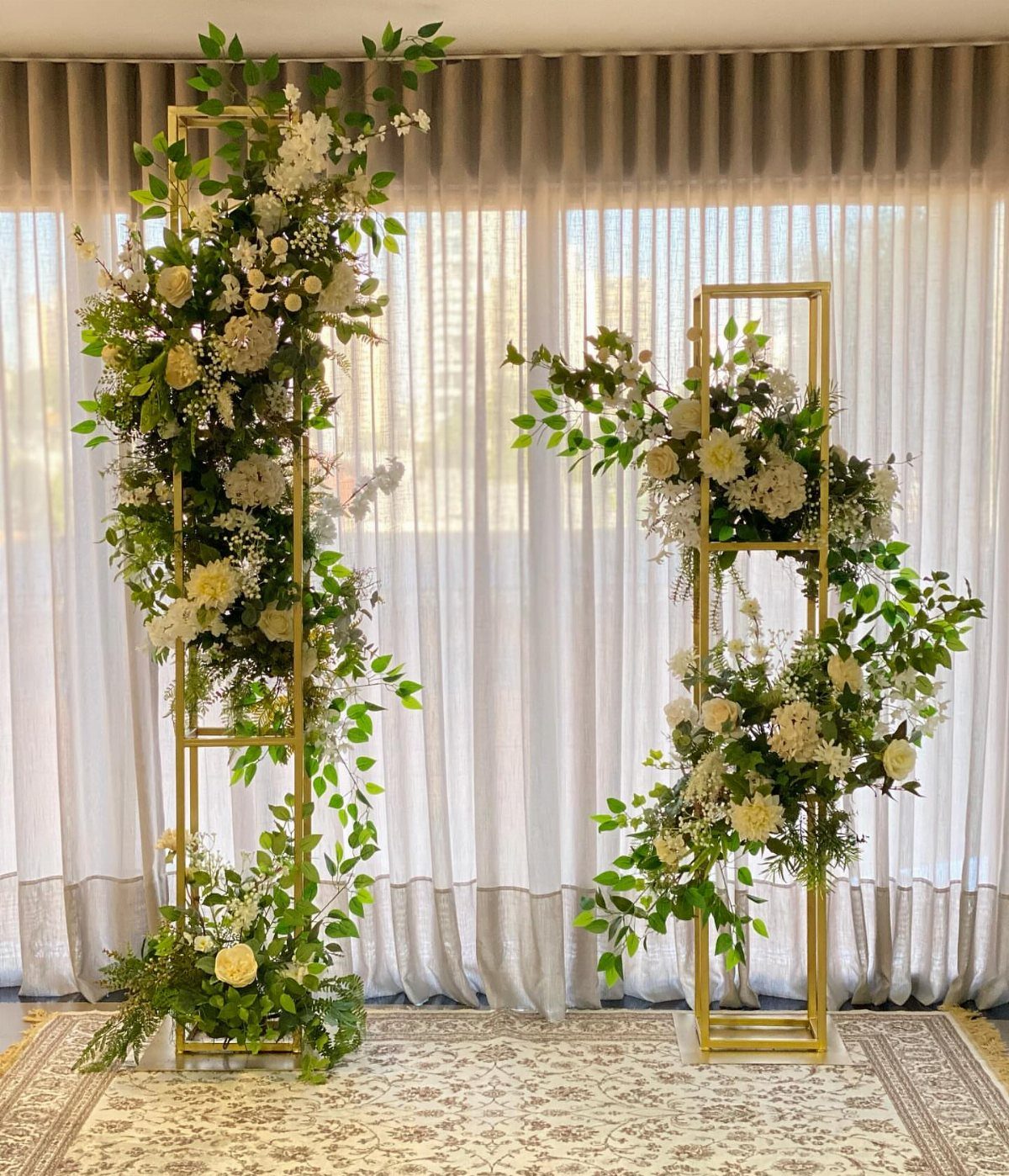 Gold rectangular frames adorned with white flowers and greenery for a wedding altar.
