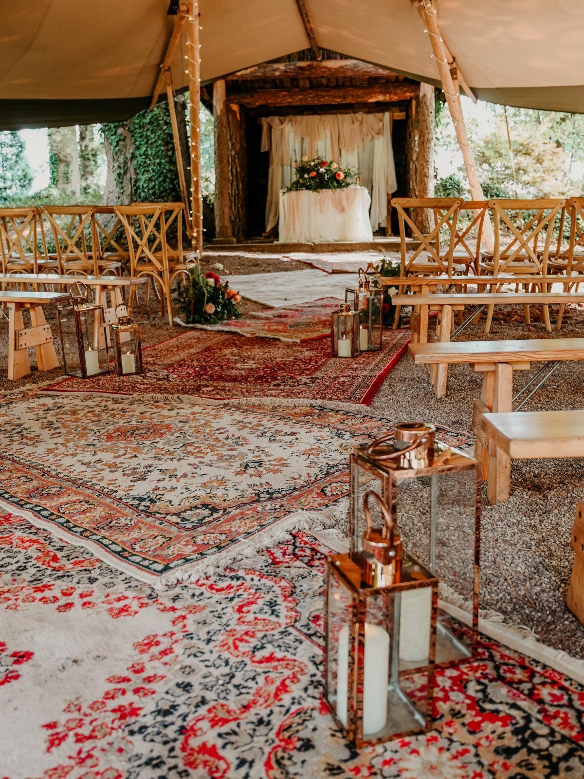 Wedding ceremony setup under a canvas tent with oriental rugs and wooden seating.