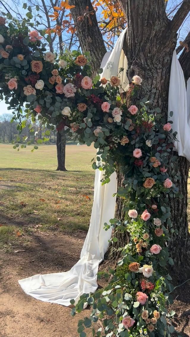 Tree trunk decorated with white fabric and pink roses for a wedding altar.