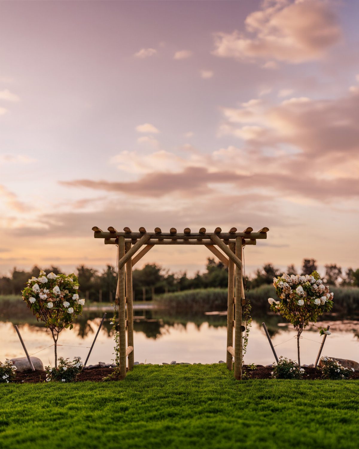 Wooden arbor structure on a green lawn overlooking a lake at sunset.