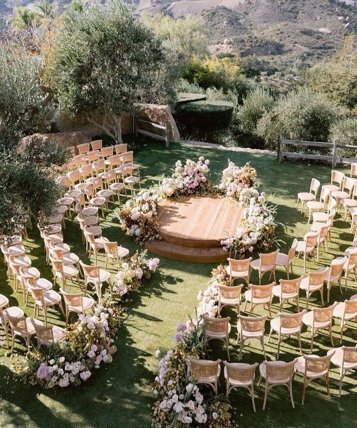 Circular wedding ceremony seating layout with light chairs and floral arrangements on grass.