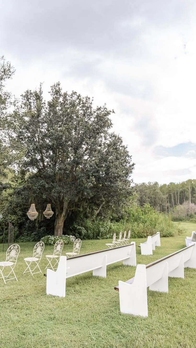 White benches and chairs arranged in rows on a grassy outdoor wedding venue.