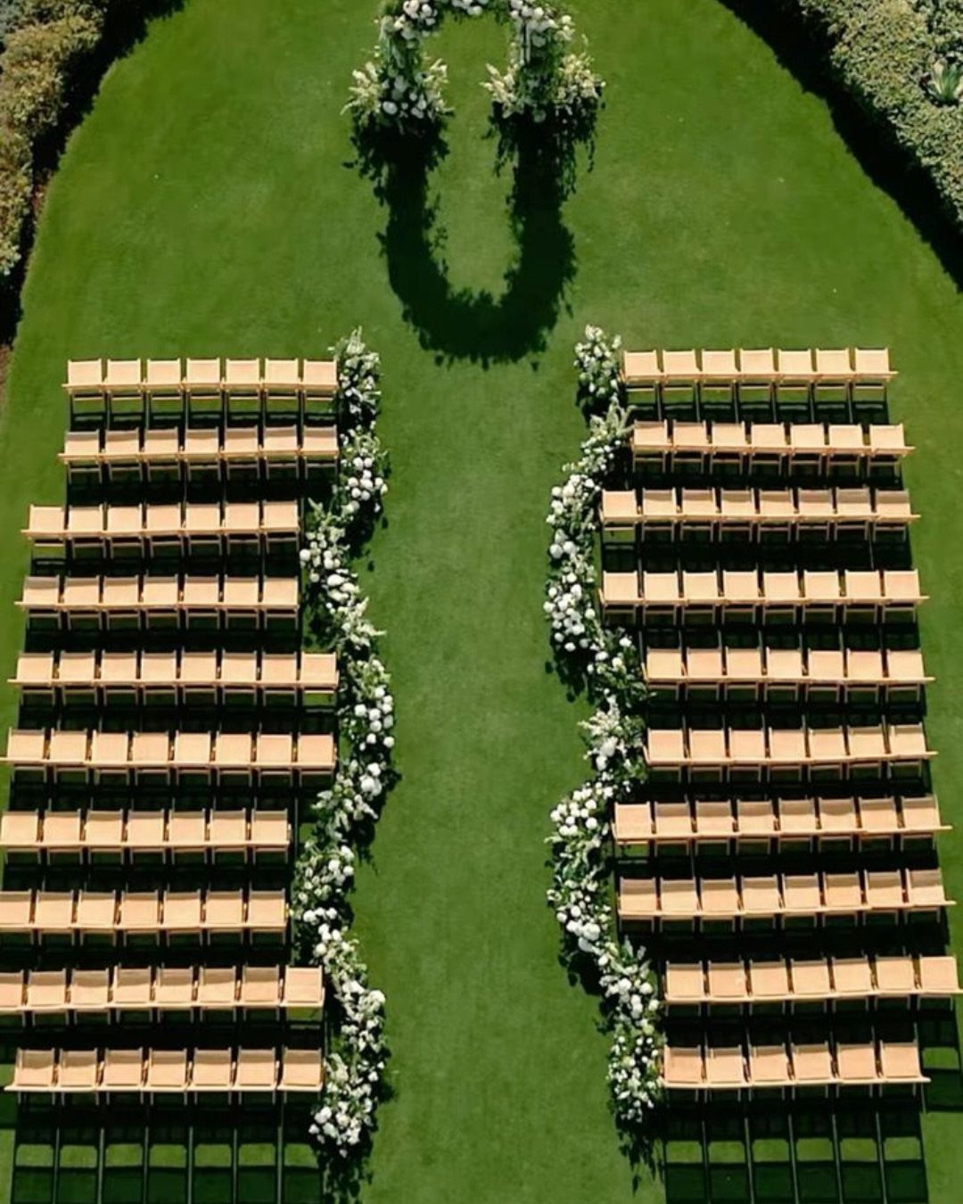 Wooden benches arranged in two sections facing a floral arch on green grass.