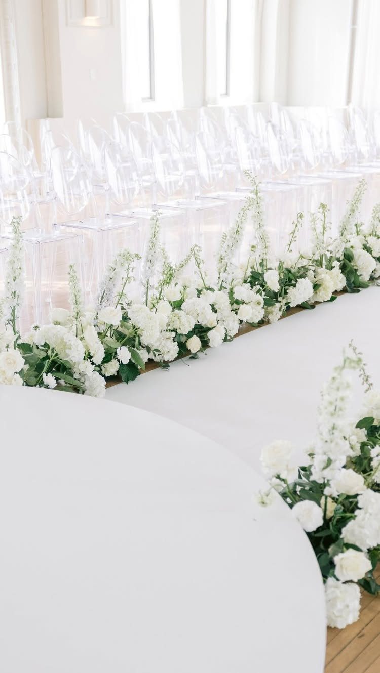 Clear acrylic chairs lined up beside a white aisle with white floral borders.