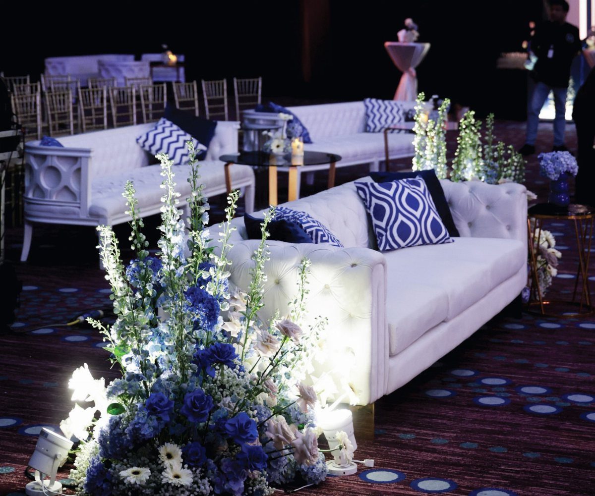 White tufted sofas with blue patterned pillows and blue floral arrangements in a lounge.
