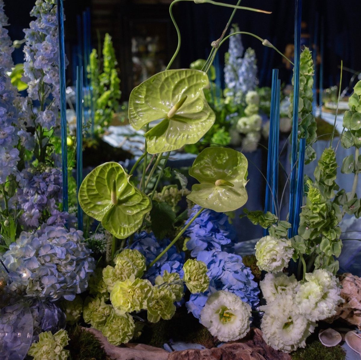 Blue hydrangeas and green anthuriums arranged with blue candles for a wedding centerpiece.