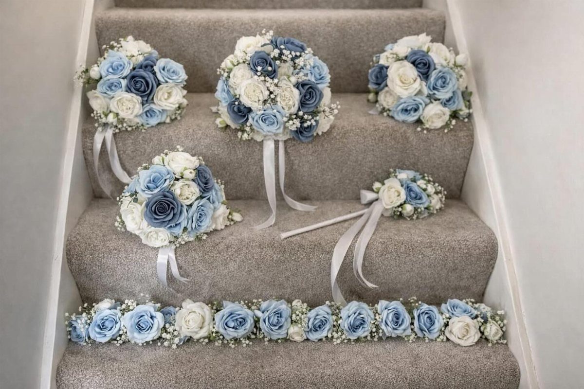 Dusty blue and white rose bouquets and garland arranged on grey carpeted stairs.