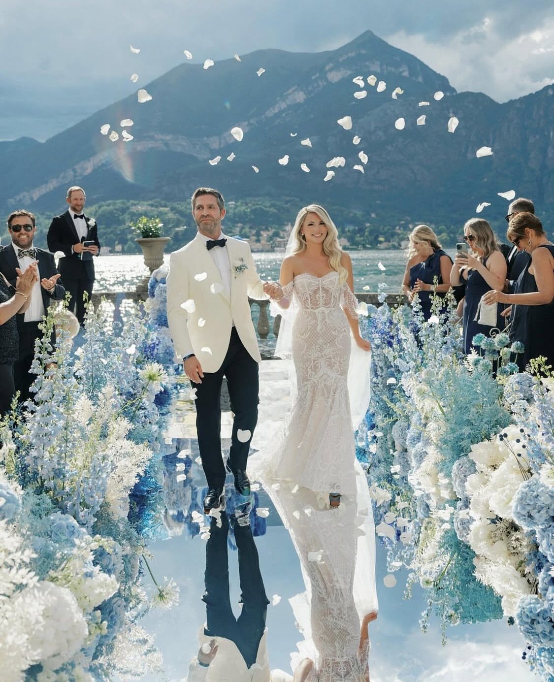 Bride and groom walking through light blue and white floral wedding arrangements outdoors.
