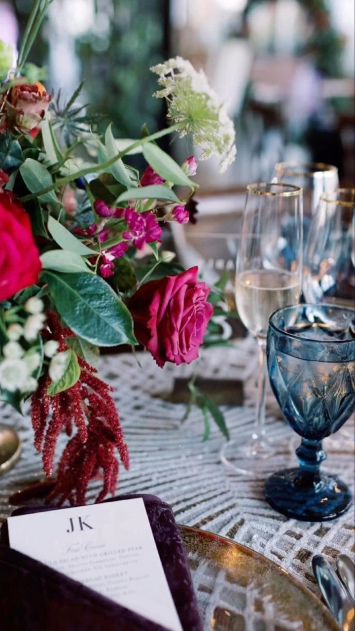 Wedding table setting with deep red roses, blue glassware, and gold charger plate.
