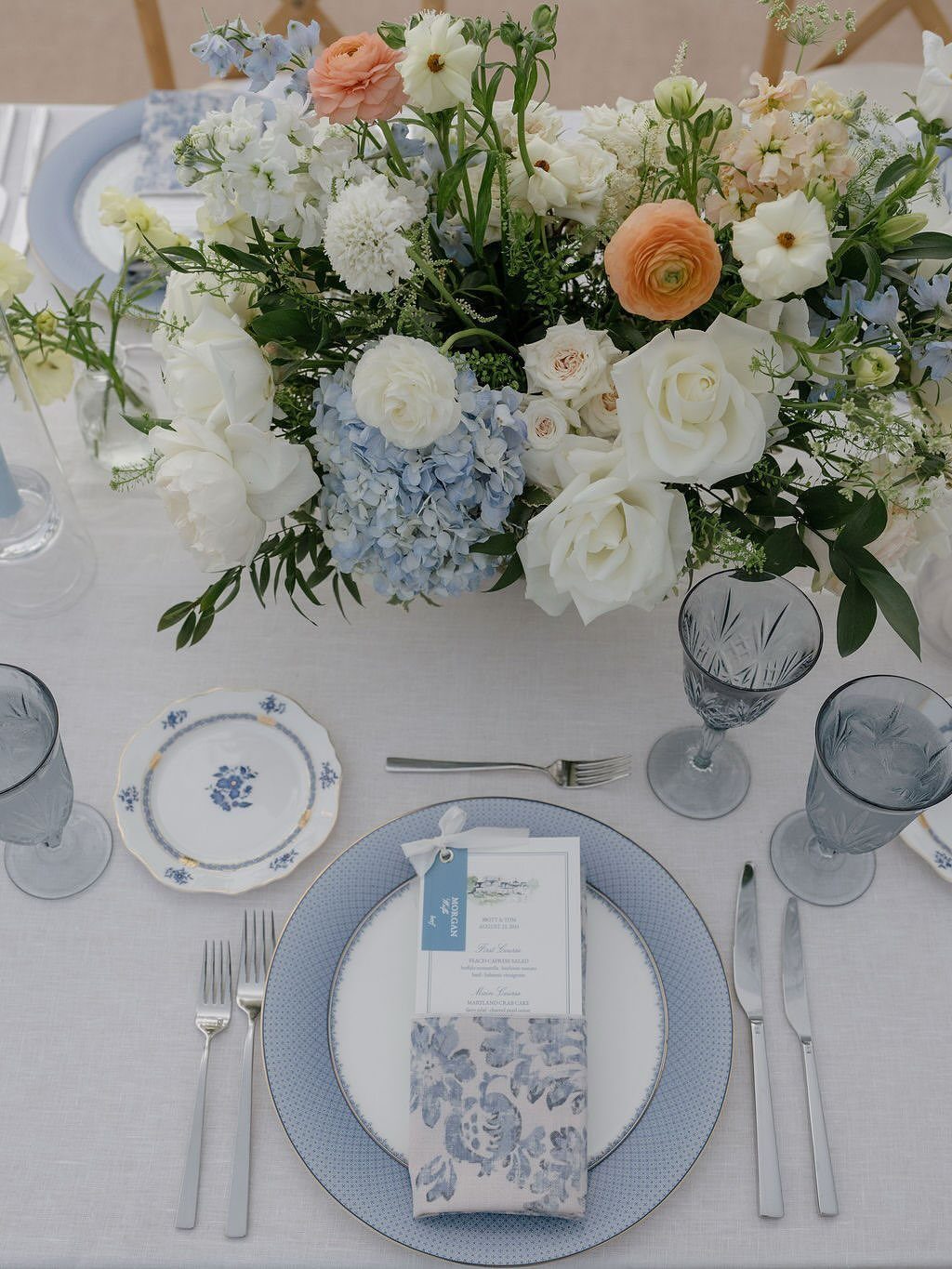 Wedding table setting with blue plates and a peach and blue floral centerpiece.