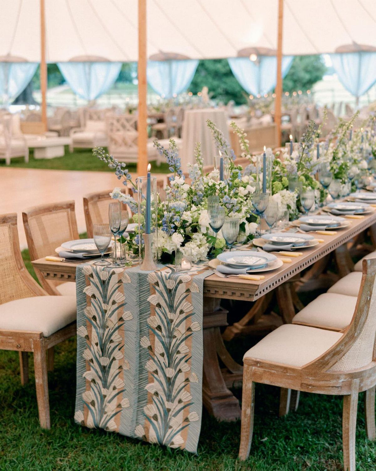 Wooden wedding table with blue and beige runner, blue glassware, and floral centerpieces.