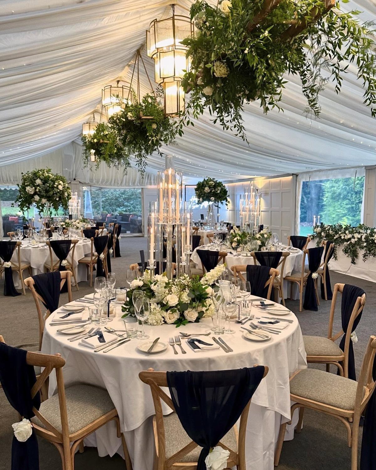 Wedding reception tables with white linens and navy blue chair sashes in a marquee