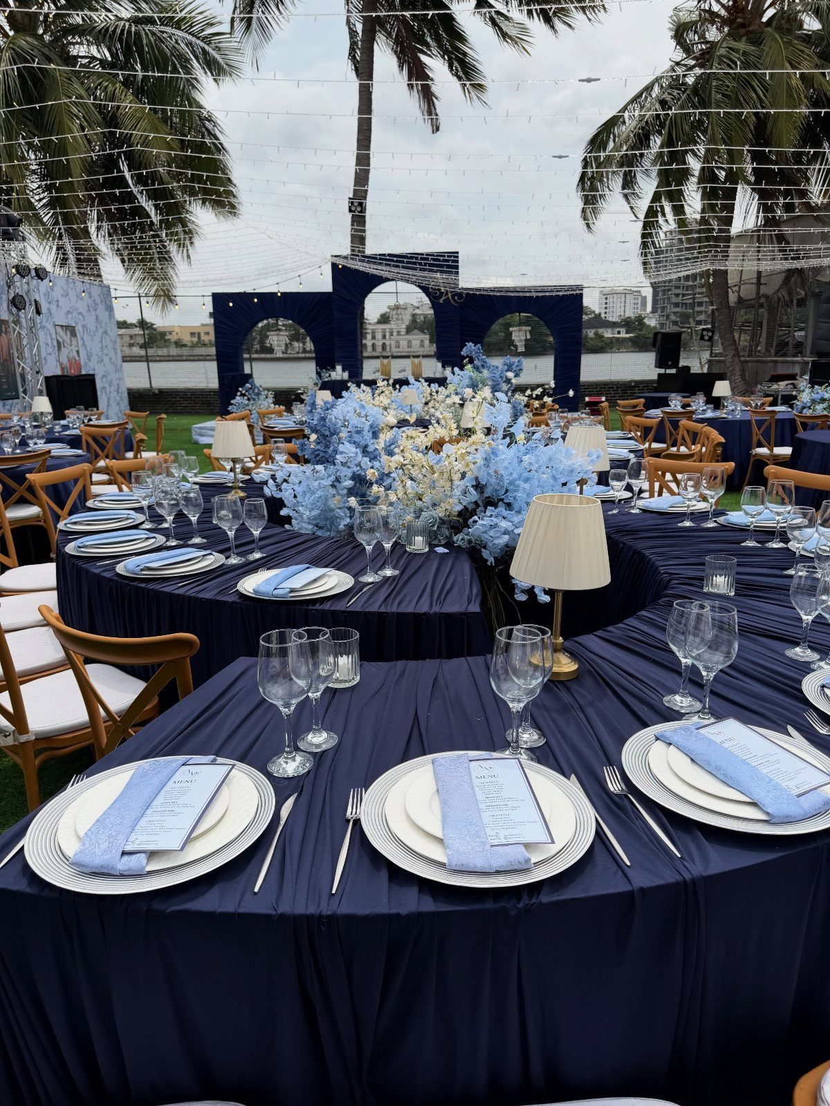 Navy blue tablecloths with light blue floral centerpieces and place settings outdoors.