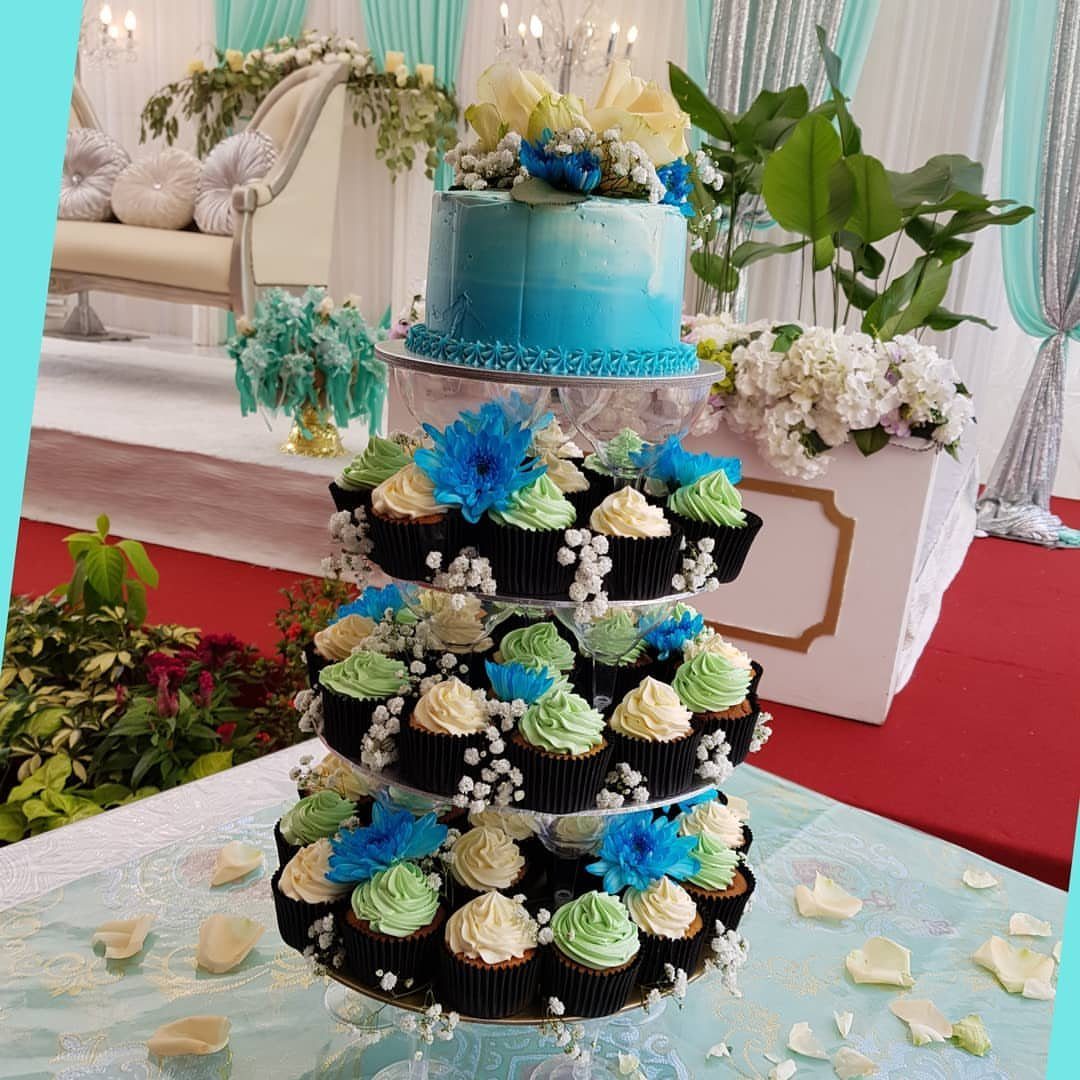 Blue cake and blue and green cupcakes on a tiered stand at a wedding.
