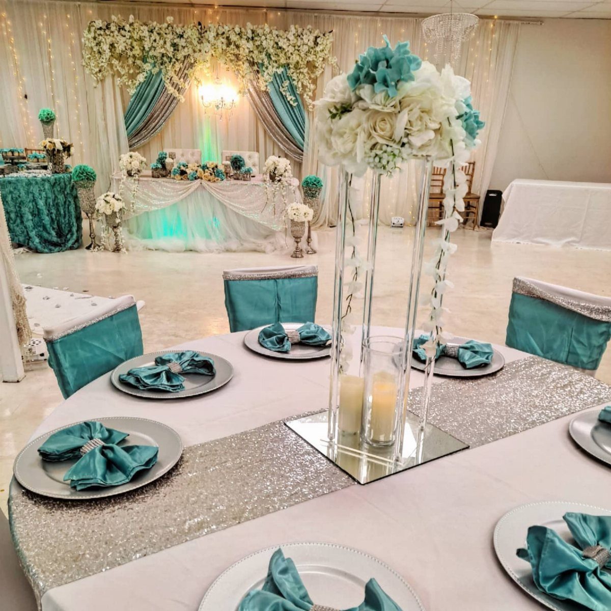 Wedding table setting with teal napkins, silver sequins, and teal floral decorations.