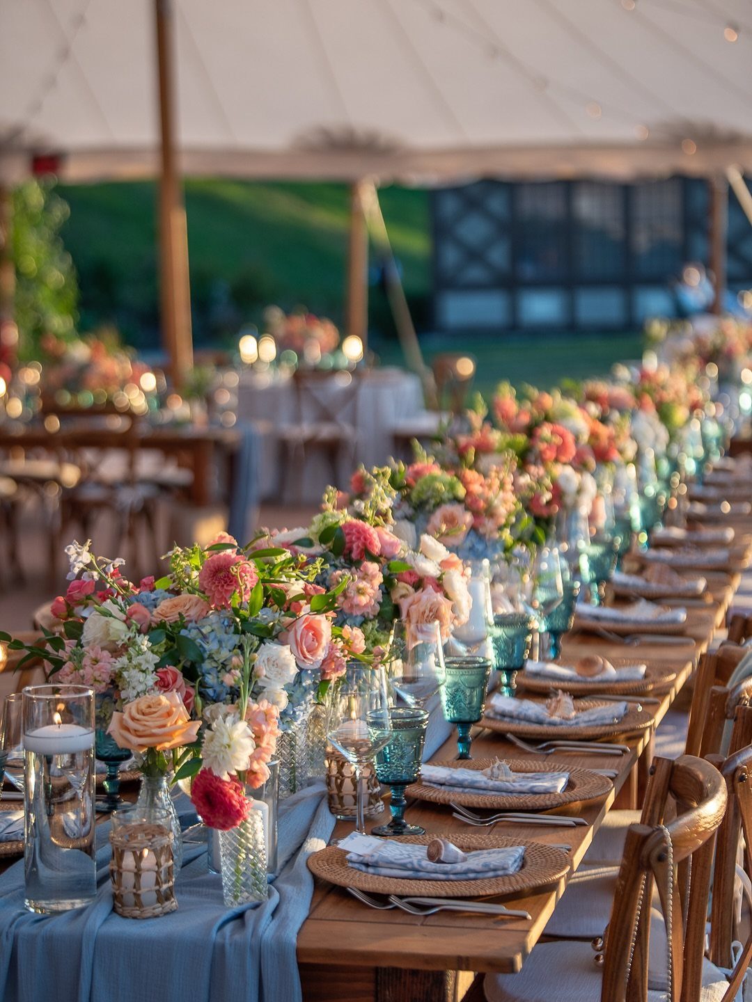 Wedding table setting with light blue linens, blue glasses, and peach floral centerpieces.