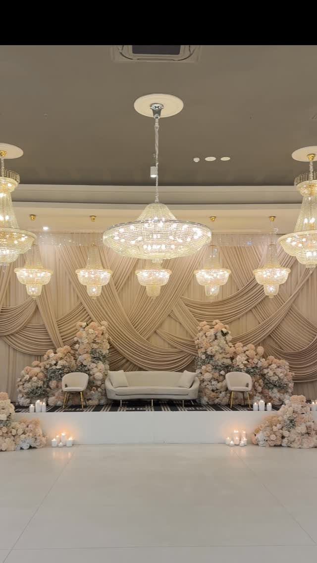 Champagne draped backdrop with blush and cream floral arrangements and crystal chandeliers.