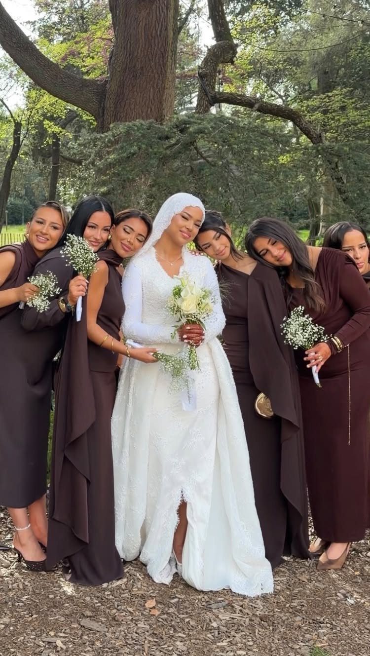 Bride in white gown and hijab with bridesmaids in chocolate brown dresses outdoors.