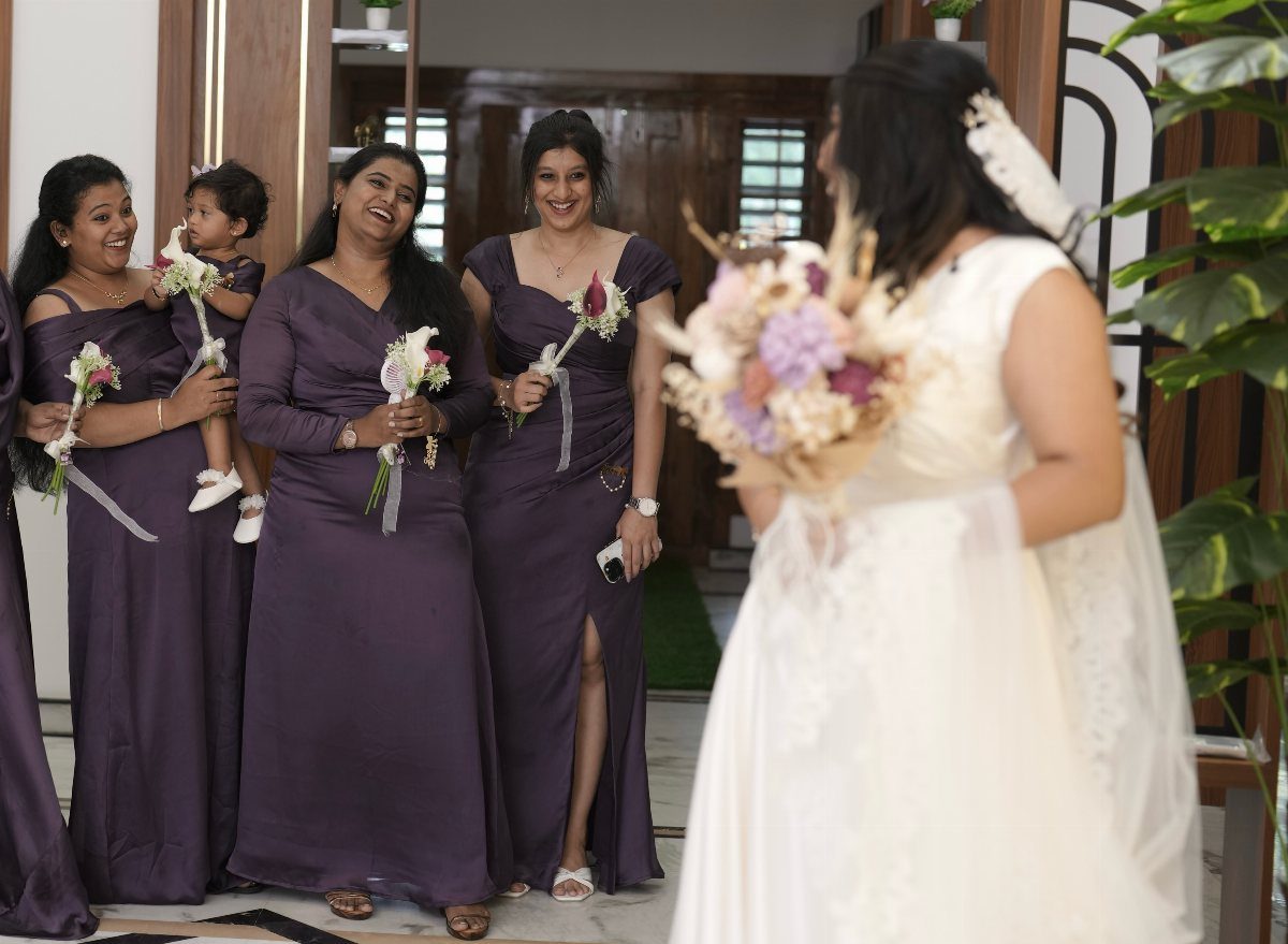Bridesmaids in deep plum gowns smiling at a bride in a white dress.