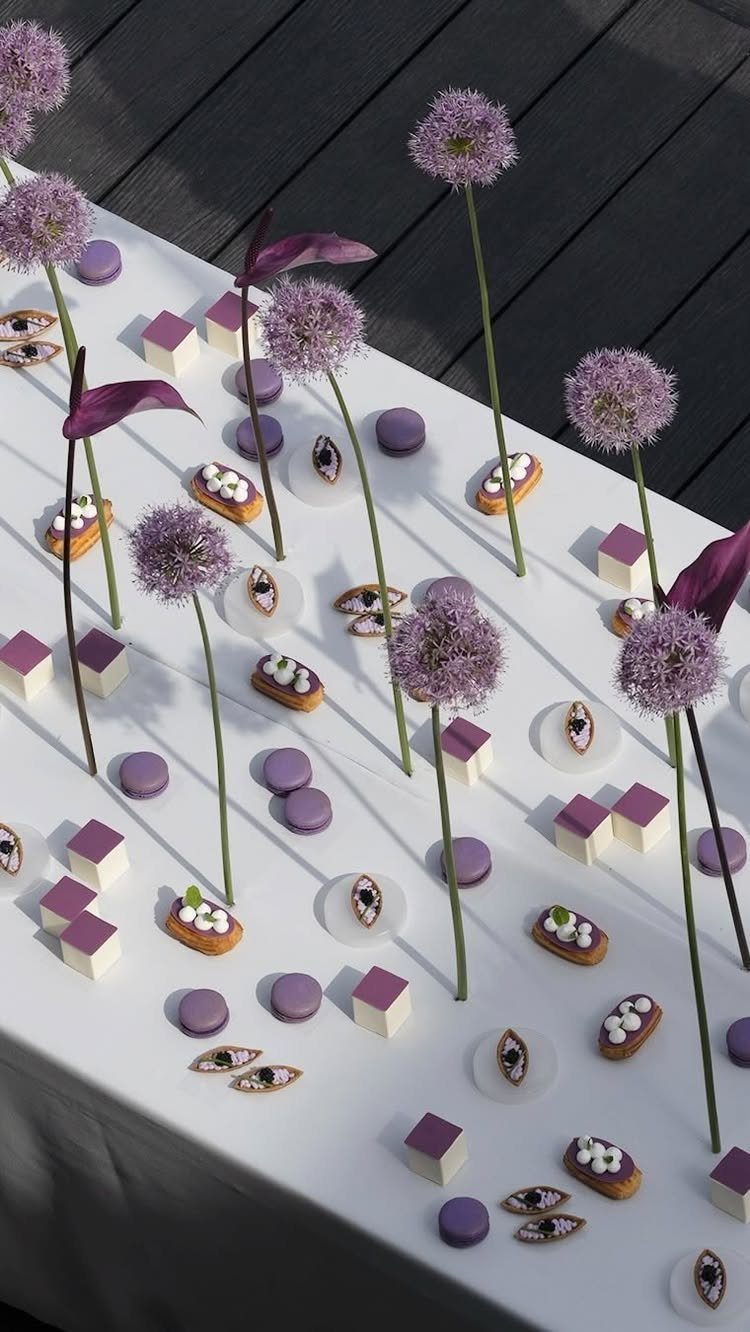 Purple allium flowers and purple desserts arranged on a white table outdoors.