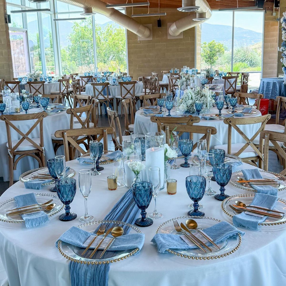 Wedding reception tables with white linens, dusty blue runners, and blue glassware.