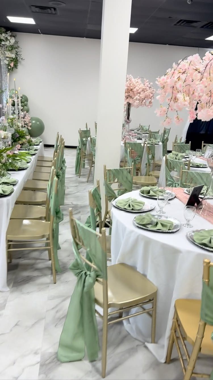 Banquet tables with white linens, gold chairs with sage green sashes, and pink flowers.