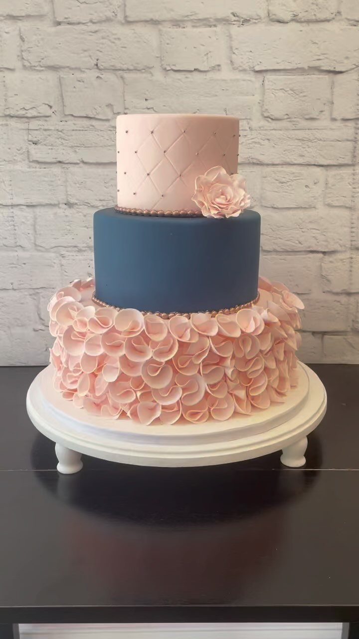 Three-tier wedding cake with navy blue and dusty rose frosting on white stand