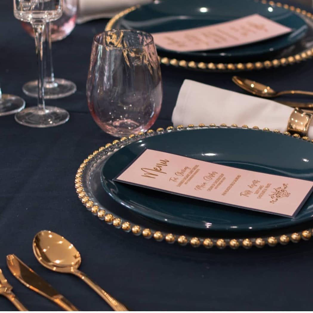 Navy blue tablecloth with teal plates, gold chargers, and blush pink menu cards.