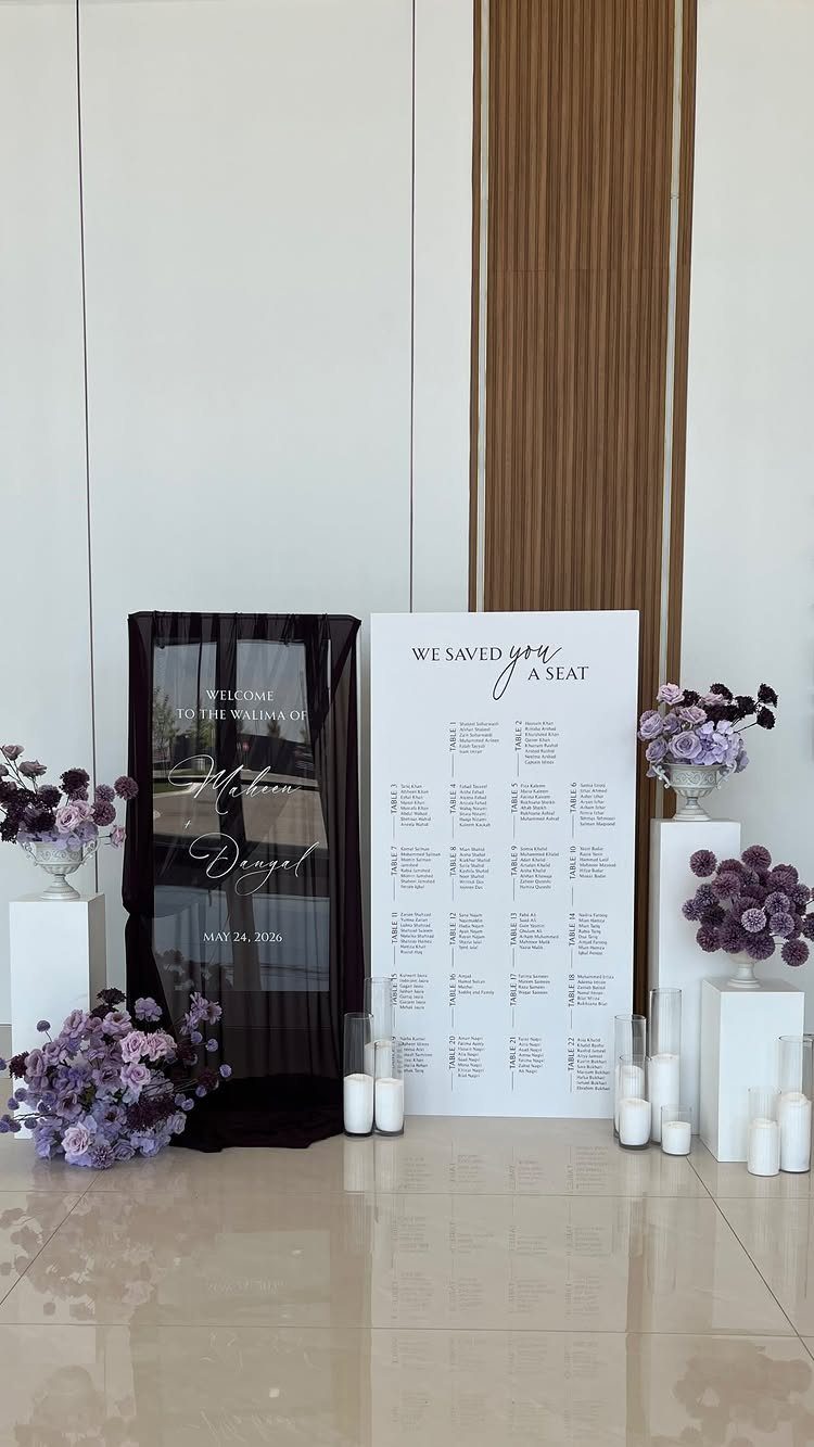 Navy blue backdrop and white seating chart with purple flowers and white candles.