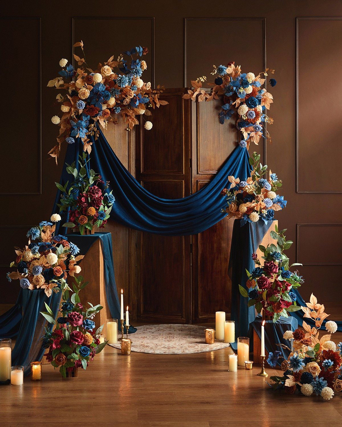 Navy blue velvet fabric draped with orange and blue floral arrangements and candles.