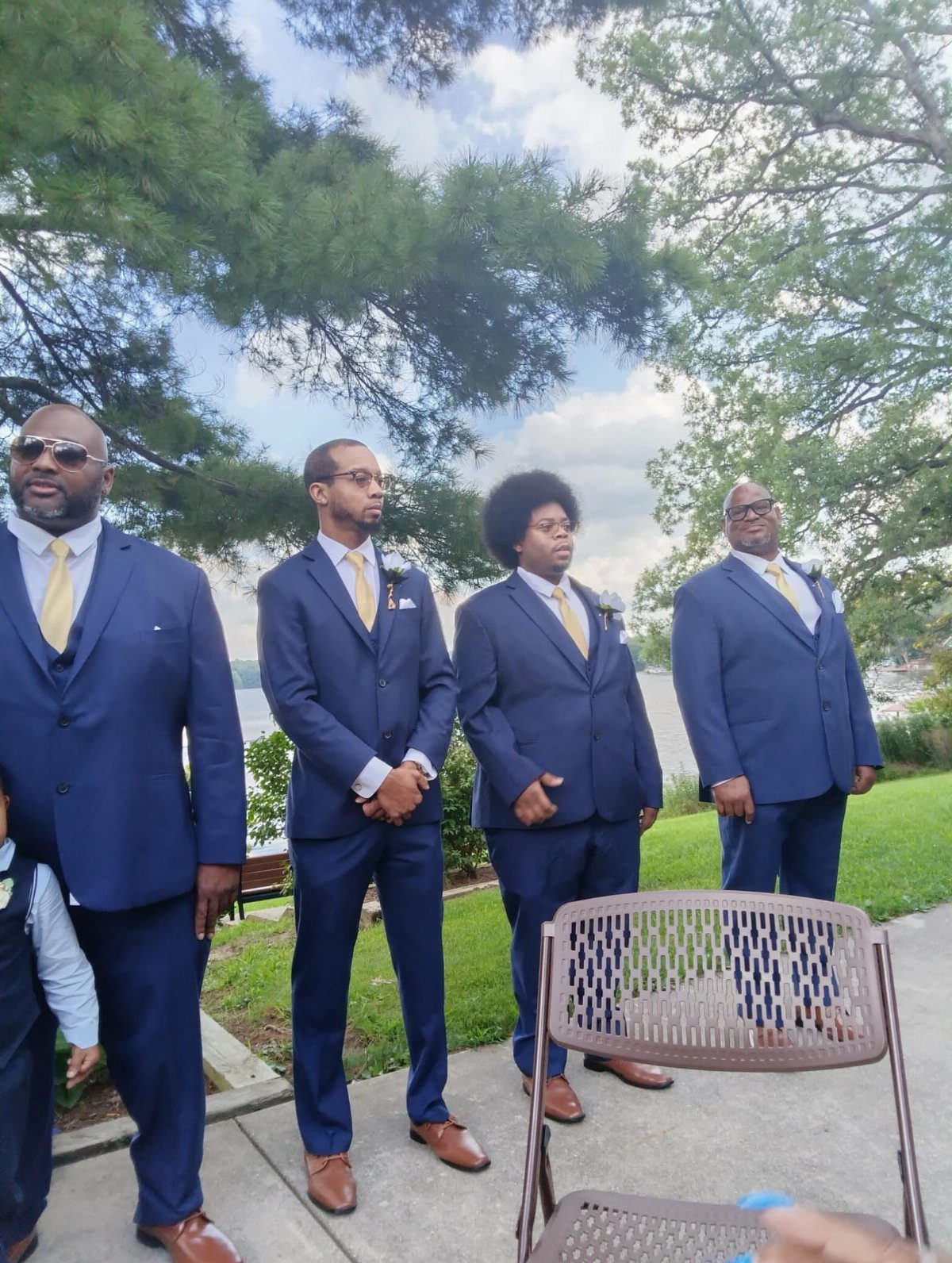 Four men in navy blue suits wearing yellow ties standing outdoors on patio