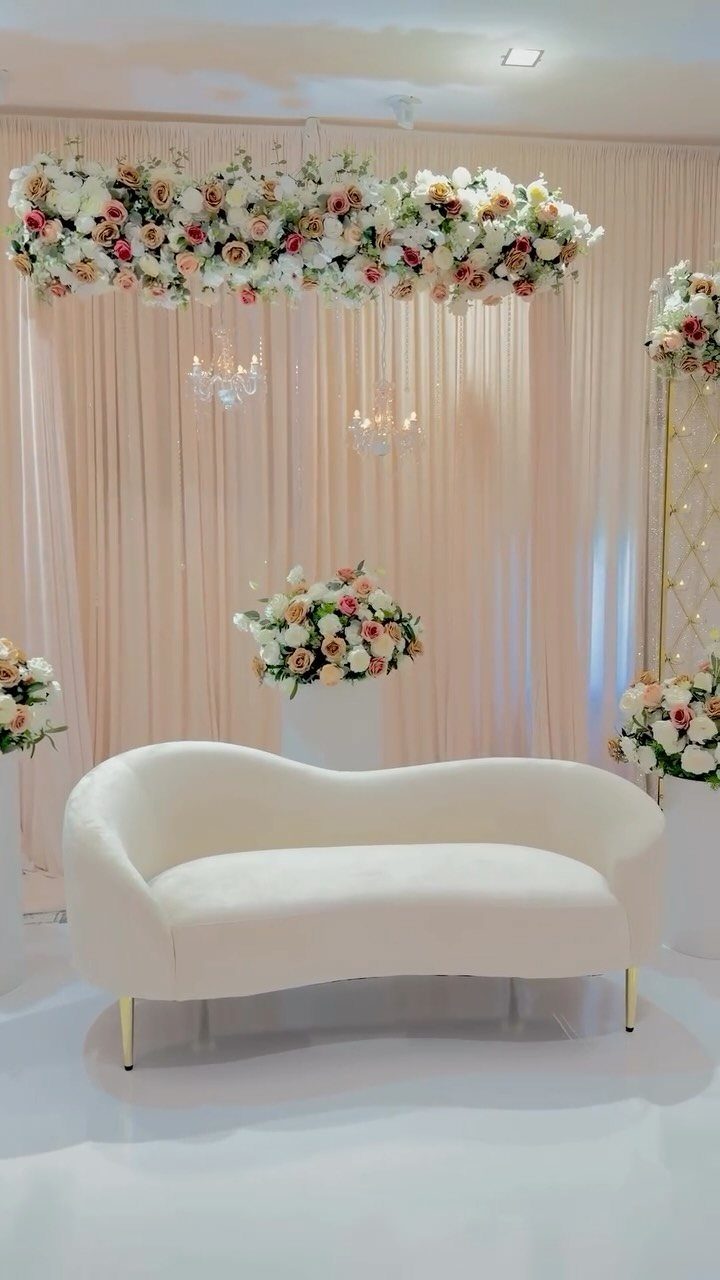 White curved sofa with champagne curtains and ivory and pink floral arrangements.