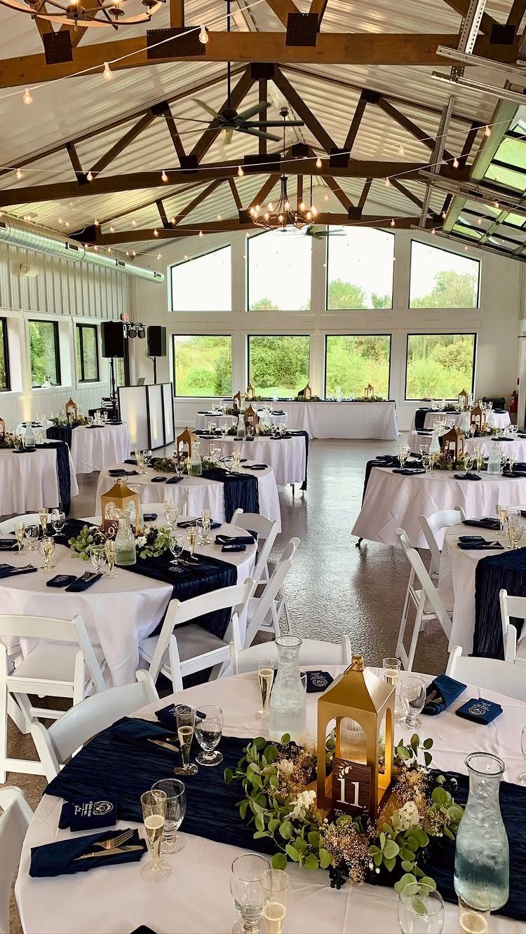 Wedding tables with white cloths, navy blue runners, and gold champagne lanterns.
